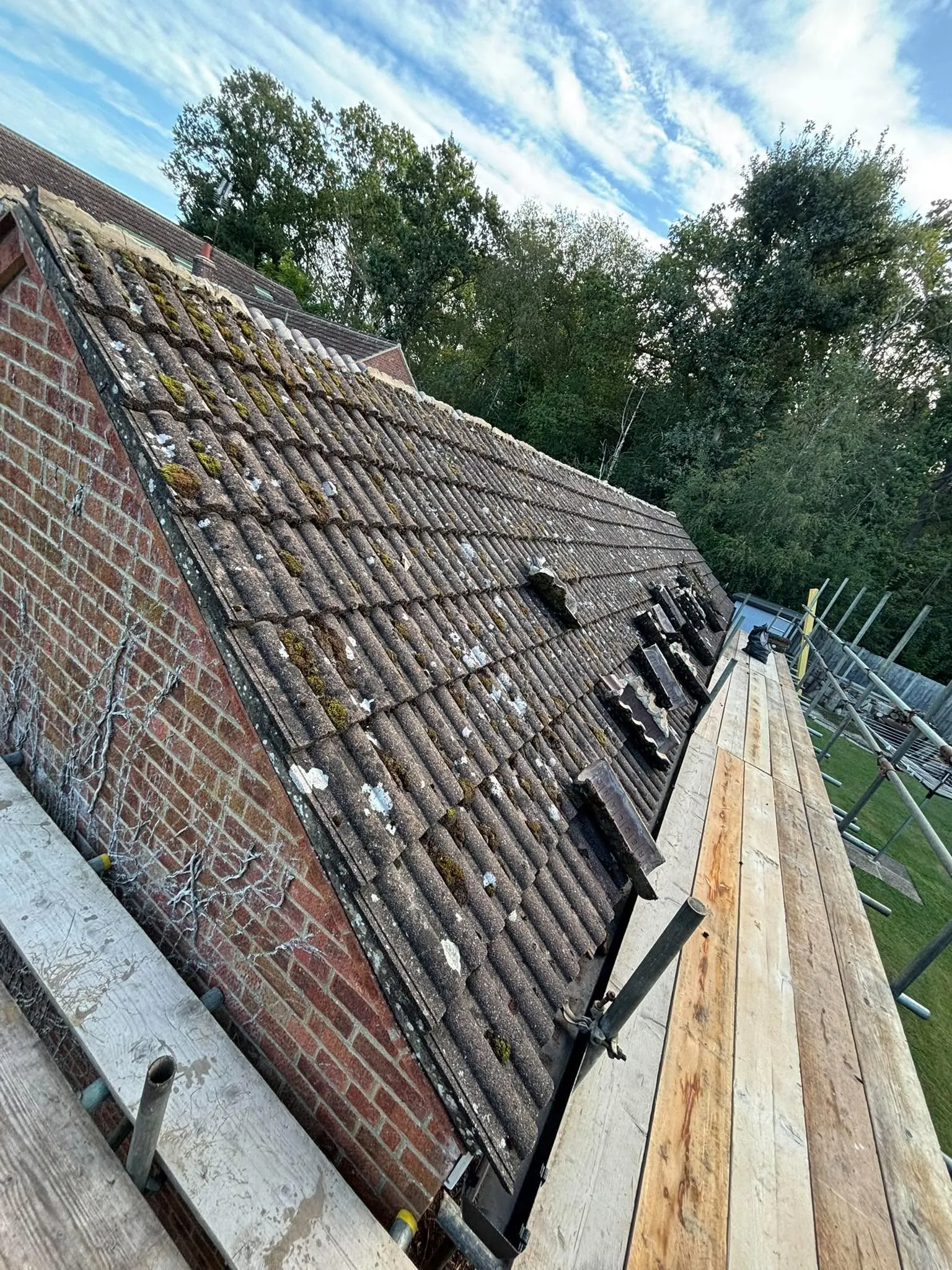 Worn tiled roof with moss growth and failing ridge before renewal